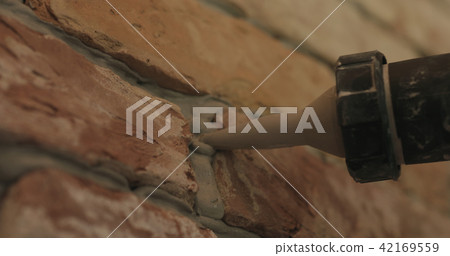 Slow motion closeup of worker filling seam between bricks with mortar from sealant gun 42169559