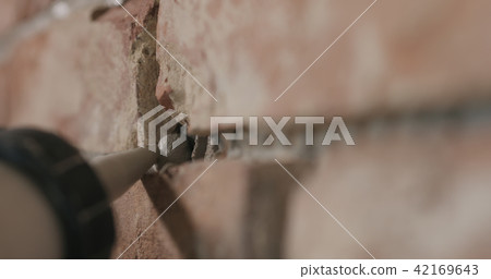 Slow motion closeup of worker filling seam between bricks with mortar from sealant gun 42169643