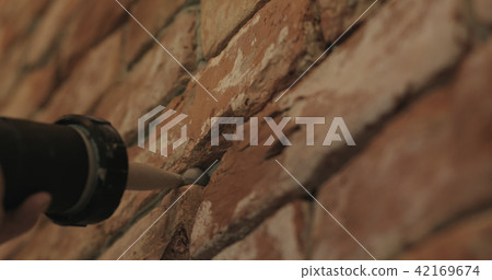 Slow motion closeup of worker filling seam between bricks with mortar from sealant gun 42169674