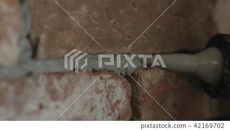 Slow motion closeup of worker filling seam between bricks with mortar from sealant gun 42169702
