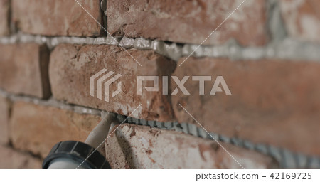 Slow motion closeup of worker filling seam between bricks with mortar from sealant gun 42169725