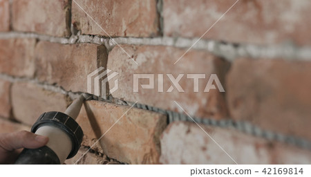 Slow motion closeup of worker filling seam between bricks with mortar from sealant gun 42169814