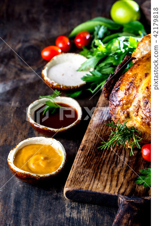 Roasted chicken with rosemary served on black plate with sauces on wooden table, top view. 42179818