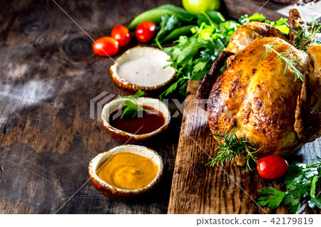 Roasted chicken with rosemary served on black plate with sauces on wooden table, top view. 42179819