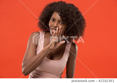 The young woman whispering a secret behind her hand over red background The young woman whispering a secret behind her hand over red background 42182361