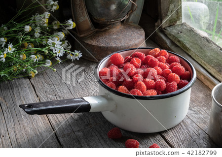 Bowl full of raspberries on wooden table. 42182799