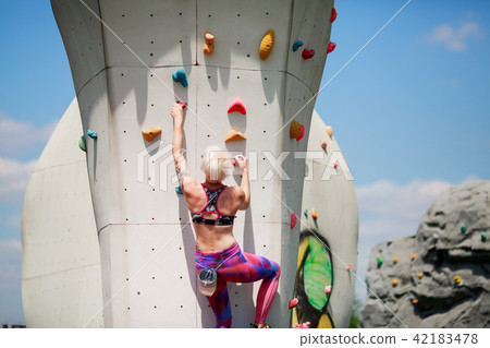 Vertical snapshot of female rock-climber, climbing up a cliff, wearing blue  leggings and a black