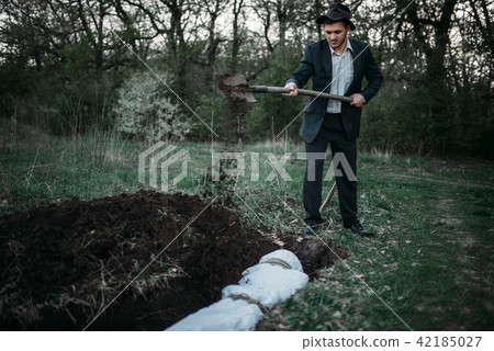 Maniac with shovel buries victim into a grave 42185027