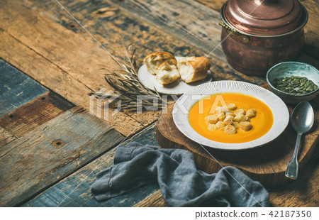 Warming pumpkin cream soup with croutons and seeds, wooden background Warming pumpkin cream soup with croutons and seeds, wooden background 42187350