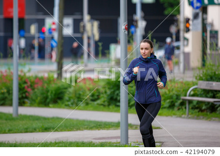 Young woman in blue jacket jogging in park 42194079