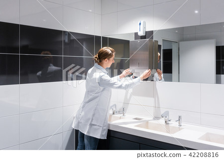 Cleaning woman refilling paper towels in public toilet Cleaning woman refilling paper towels in public toilet 42208816