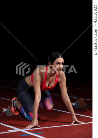 woman sprinter leaving starting blocks on the athletic track. exploding start on stadium with 42210923