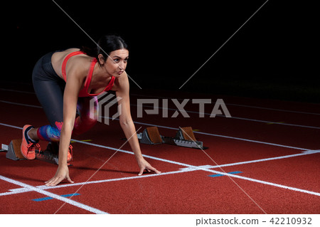 woman sprinter leaving starting blocks on the athletic track. exploding start on stadium with woman sprinter leaving starting blocks on the athletic track. exploding start on stadium with 42210932