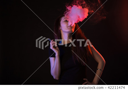 Young woman in neon light and smoke of e-cigarettes or vape on black background Young woman in neon light and smoke of e-cigarettes or vape on black background 42211474