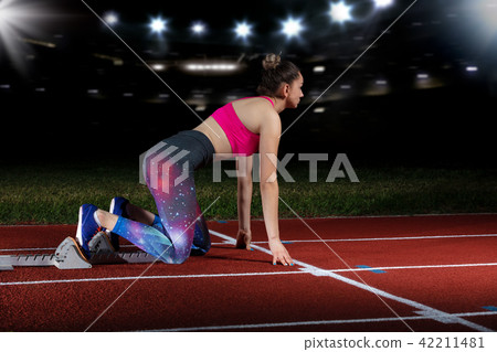 woman sprinter leaving starting blocks on the athletic track. exploding start on stadium with 42211481