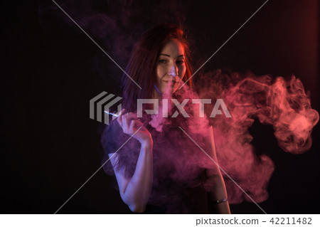 Portrait of asian woman smoking vape or e-cigarette in neon light at black background. Portrait of asian woman smoking vape or e-cigarette in neon light at black background. 42211482