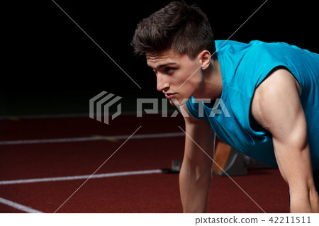 Sprinter leaving starting blocks on the running track in front of big modern stadium with lights Sprinter leaving starting blocks on the running track in front of big modern stadium with lights 42211511