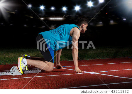 Sprinter leaving starting blocks on the running track in front of big modern stadium with lights Sprinter leaving starting blocks on the running track in front of big modern stadium with lights 42211522