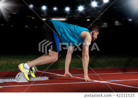 Sprinter leaving starting blocks on the running track in front of big modern stadium with lights Sprinter leaving starting blocks on the running track in front of big modern stadium with lights 42211525
