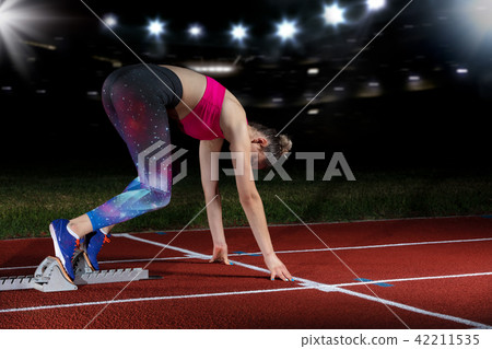 woman sprinter leaving starting blocks on the athletic track. exploding start on stadium with 42211535