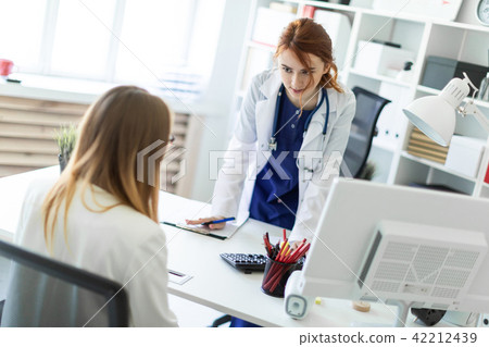 A beautiful young girl in a white robe is standing near a computer desk in the office and 42212439