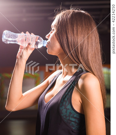 Fitness young woman drinking water in the gym. Muscular woman taking break after exercise 42214250