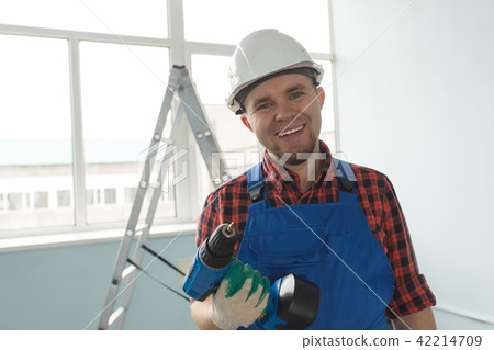 Happy builder standing with drill infront of window. 42214709