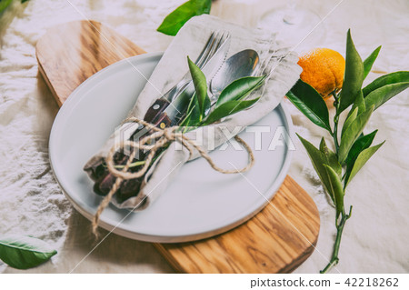 Table setting with white plate, cutlery, linen napkin and orange tree branch decoration on white 42218262