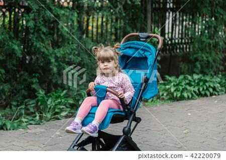 Little girl is sitting in a pram in a beautiful 42220079