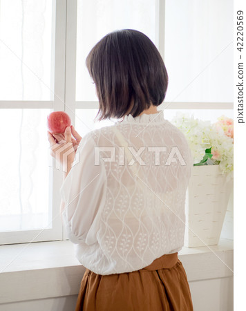 Girl eating fruit by the window Girl eating fruit by the window 42220569