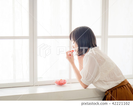 Girl eating fruit by the window Girl eating fruit by the window 42221102