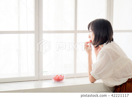 Girl eating fruit by the window Girl eating fruit by the window 42221117
