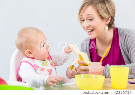 happy mother giving a fresh and nutritious banana to her cute baby girl 42225725