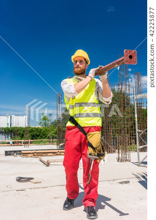 Blue-collar worker carrying a heavy metallic bar during work 42225877