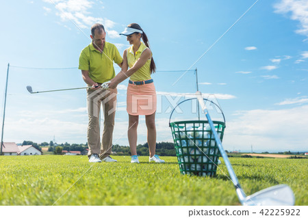 Cheerful young woman learning the correct grip and move for using the golf club Cheerful young woman learning the correct grip and move for using the golf club 42225922