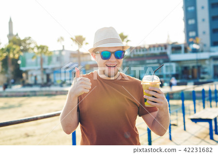lifestyle, drinks and people concept - man in sunglasses drinking coffee frappe from disposable 42231682