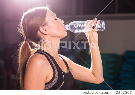 Fitness young woman drinking water in the gym. Muscular woman taking break after exercise 42232507
