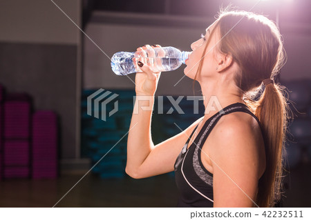 Fitness young woman drinking water in the gym. Muscular woman taking break after exercise 42232511