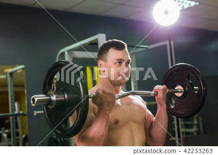 Muscular young man lifting weights in gym Muscular young man lifting weights in gym 42233263