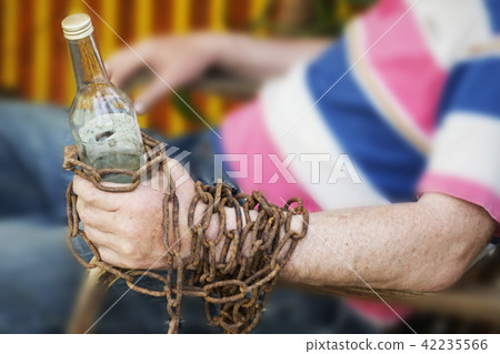 Hand chained to a bottle of alcohol, a man sitting in a chair 42235566