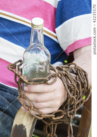 Hand chained to a bottle of alcohol, a man sitting in a chair Hand chained to a bottle of alcohol, a man sitting in a chair 42235570