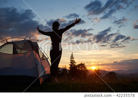 Rear view silhouette of female standing with open arms near camping in mountains at sunrise 42235578