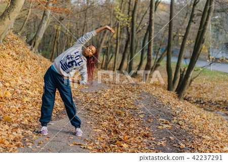 Full-length view of the young sportive african woman stretching in the autumn park. Full-length view of the young sportive african woman stretching in the autumn park. 42237291