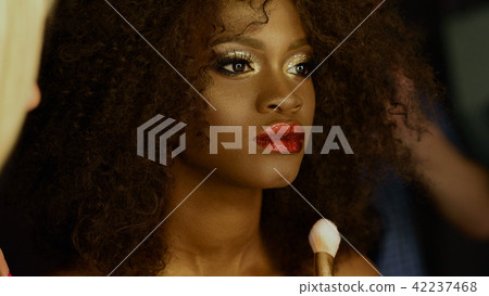 Side portrait of the thoughtful african lady with bright make-up. She is receiving professional make Side portrait of the thoughtful african lady with bright make-up. She is receiving professional make 42237468