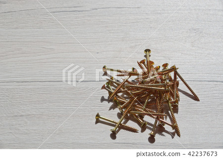 Pile of yellow screws on wooden background Pile of yellow screws on wooden background 42237673