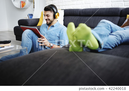 Couple Lying On Sofa With Tablet PC and Earphones Couple Lying On Sofa With Tablet PC and Earphones 42240018