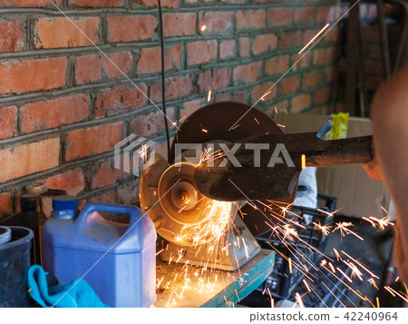 farmer sharpens a shovel on electric grindstone 42240964