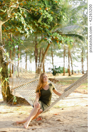 Young nice girl sitting barefoot on wicker hammock, sand and trees in background. Young nice girl sitting barefoot on wicker hammock, sand and trees in background. 42263200