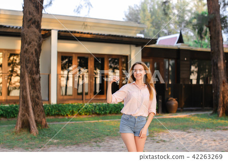 Young woman standing near resort house and keeping keys. Young woman standing near resort house and keeping keys. 42263269