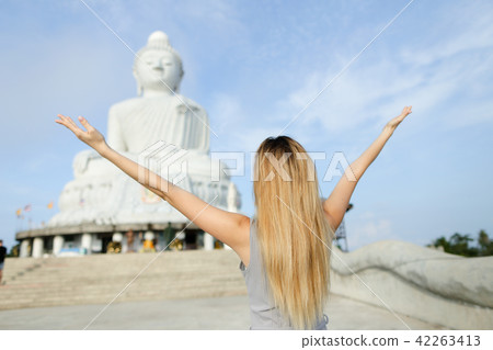 Young blonde girl with outstretched arms standing near concrete statue of Buddha in Phuket. Young blonde girl with outstretched arms standing near concrete statue of Buddha in Phuket. 42263413